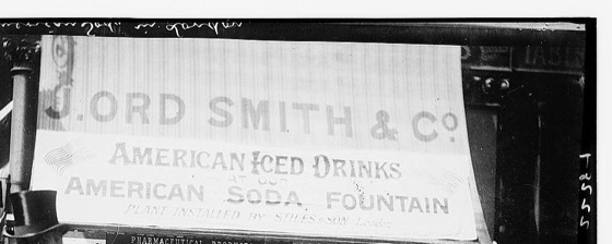 Recorte cinematográfico do storefront J. Ord Smith & Co. (mesma fonte da cena 6 e 7)