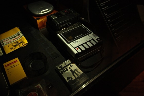 Vitrine de museu com gravador cassette de mesa e fitas (anos 1970/80)