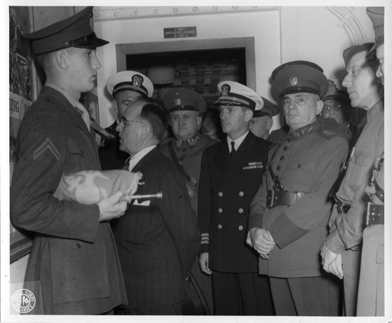 Original caption: "President Getulio Vargas, President of Brazil, is shown speaking through the ship's loud speaker on the USAT General William A. Mann to give a greeting to the Brazilian troops. Paul S. Maguire, Captain of the transport, is shown looking on. In the background is General Enrico Gasp