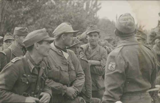 Um soldado brasileiro, com a insígnia da cobra fumando, se dirige a prisioneiros alemães em Collecchio, 29 de abril de 1945.